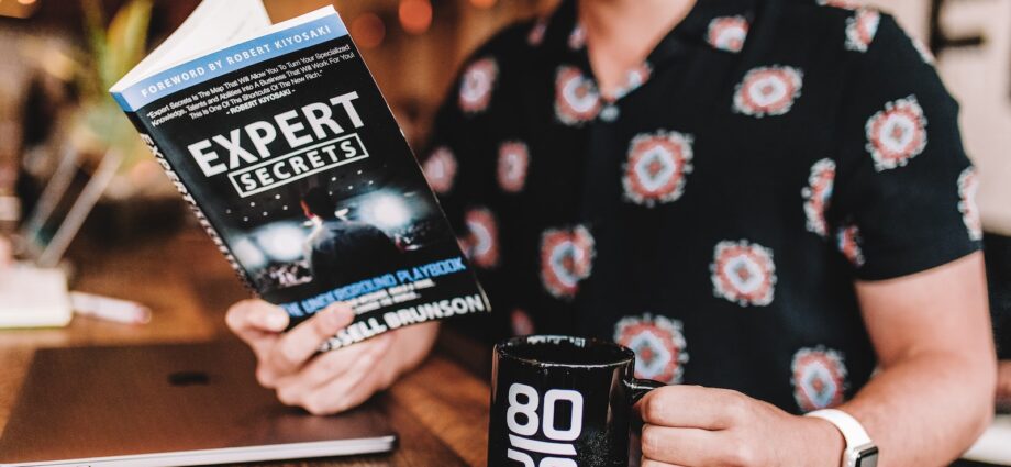 smiling man reading book while holding mug